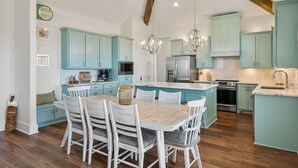 Une cuisine moderne avec des meubles de couleur turquoise, une table à manger en bois et des luminaires suspendus.