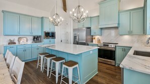 Une cuisine avec des meubles de couleur bleu clair, un grand îlot central doté de tabourets, des appareils électroménagers en acier inoxydable et des luminaires suspendus.