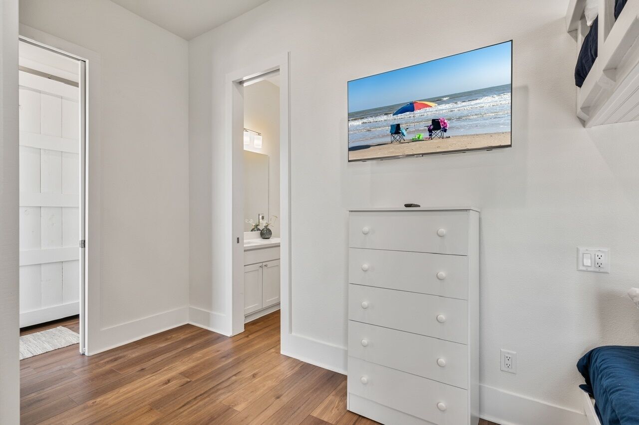 A bedroom with a bed, a dresser, and a wall-mounted TV displaying a beach scene.
