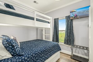 A bedroom with bunk beds, a window with curtains, a TV on the wall, and a small shelf with items.