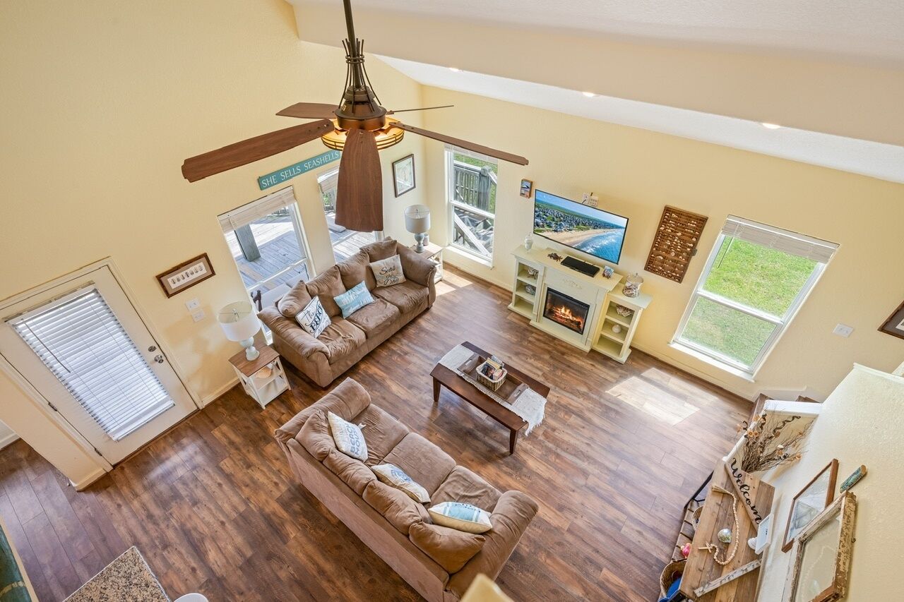 A spacious living room with a ceiling fan, a fireplace, a television, and a large window.