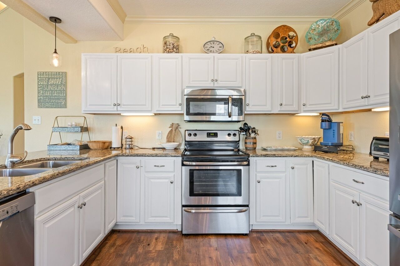 Una cocina con armarios blancos, electrodomésticos de acero inoxidable y suelo de madera.