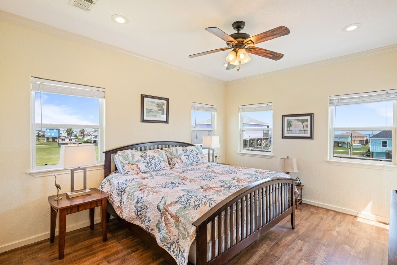 A bedroom with a bed, ceiling fan, and windows with blinds.