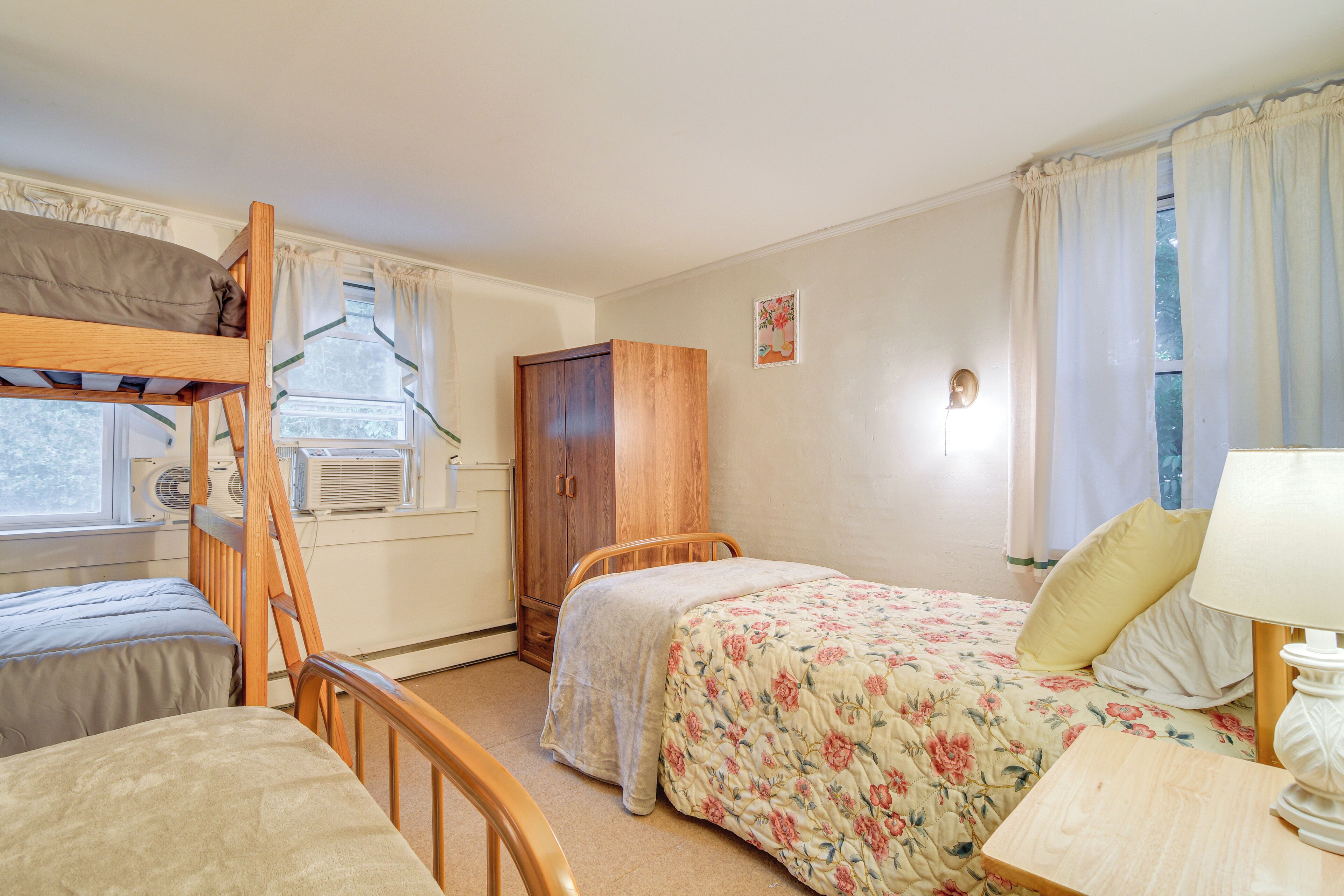 Una habitación con literas, un armario de madera, una colcha de flores y una mesita de noche con lámpara.