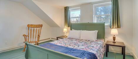 A bedroom with a green bed, a wooden chair, two bedside tables with lamps, and a window with curtains.