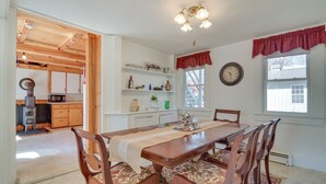 A dining area with a wooden table and chairs, a chandelier, and a view of the kitchen. - Lakefront Maine House ~ 4 Mi to Colby College (Oakland)