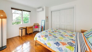A bedroom with a wooden floor, a bed with a colorful patterned bedspread, a chair, a lamp, a window, and a door. - Waterfront New York Getaway w/ Kayaks (Riverhead)