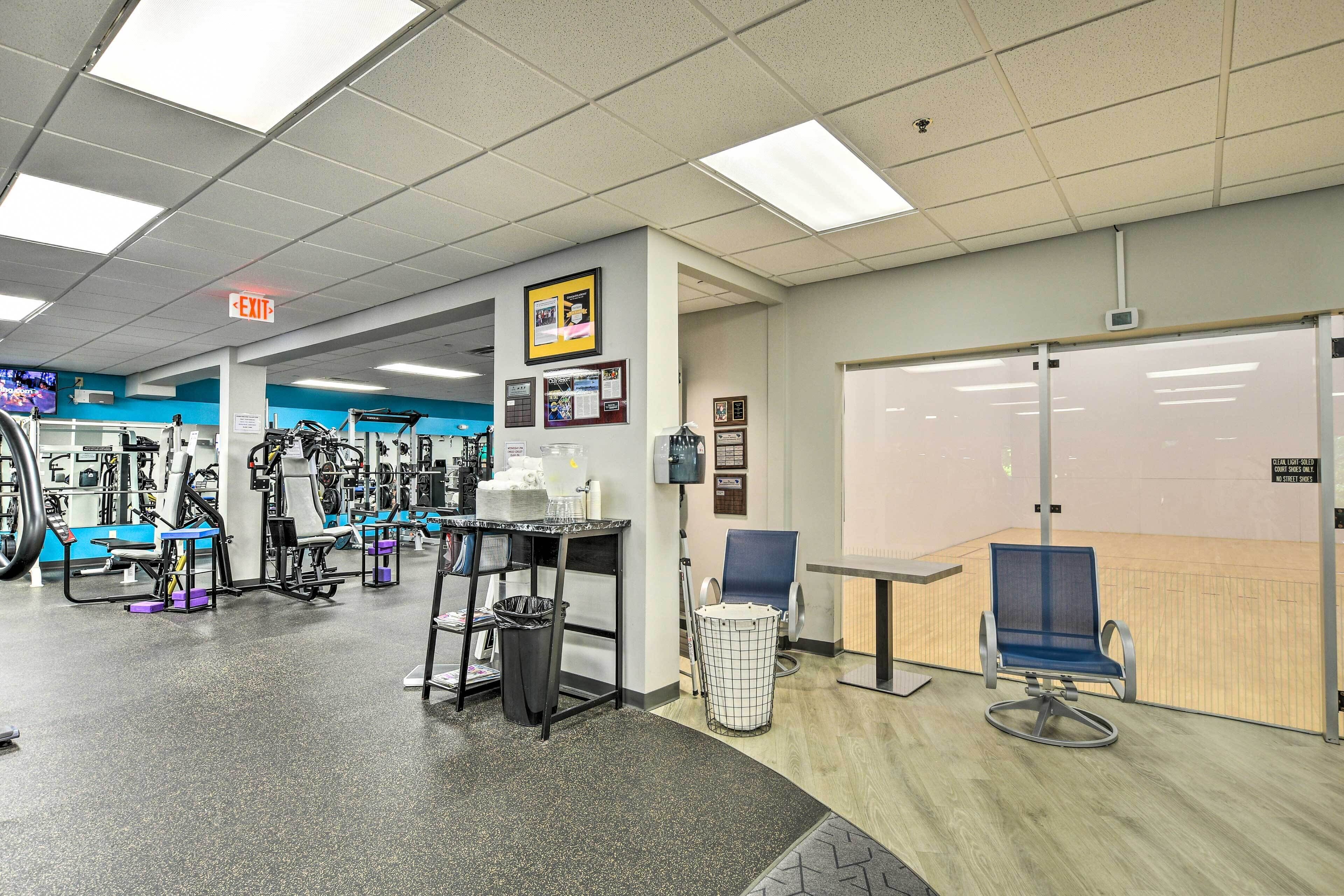 A gym with exercise equipment, a trash bin, a chair, and an exit sign.