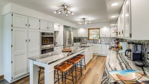 A kitchen with white cabinets, a marble countertop, and a central island with stools. - Tranquil Lakefront Greers Ferry Escape w/ Fire Pit (Higden)