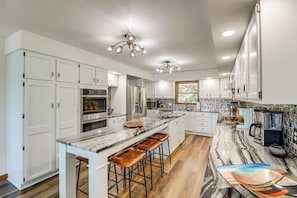 A modern kitchen with white cabinets, a marble countertop, and a central island with stools. - Tranquil Lakefront Greers Ferry Escape w/ Fire Pit (Higden)