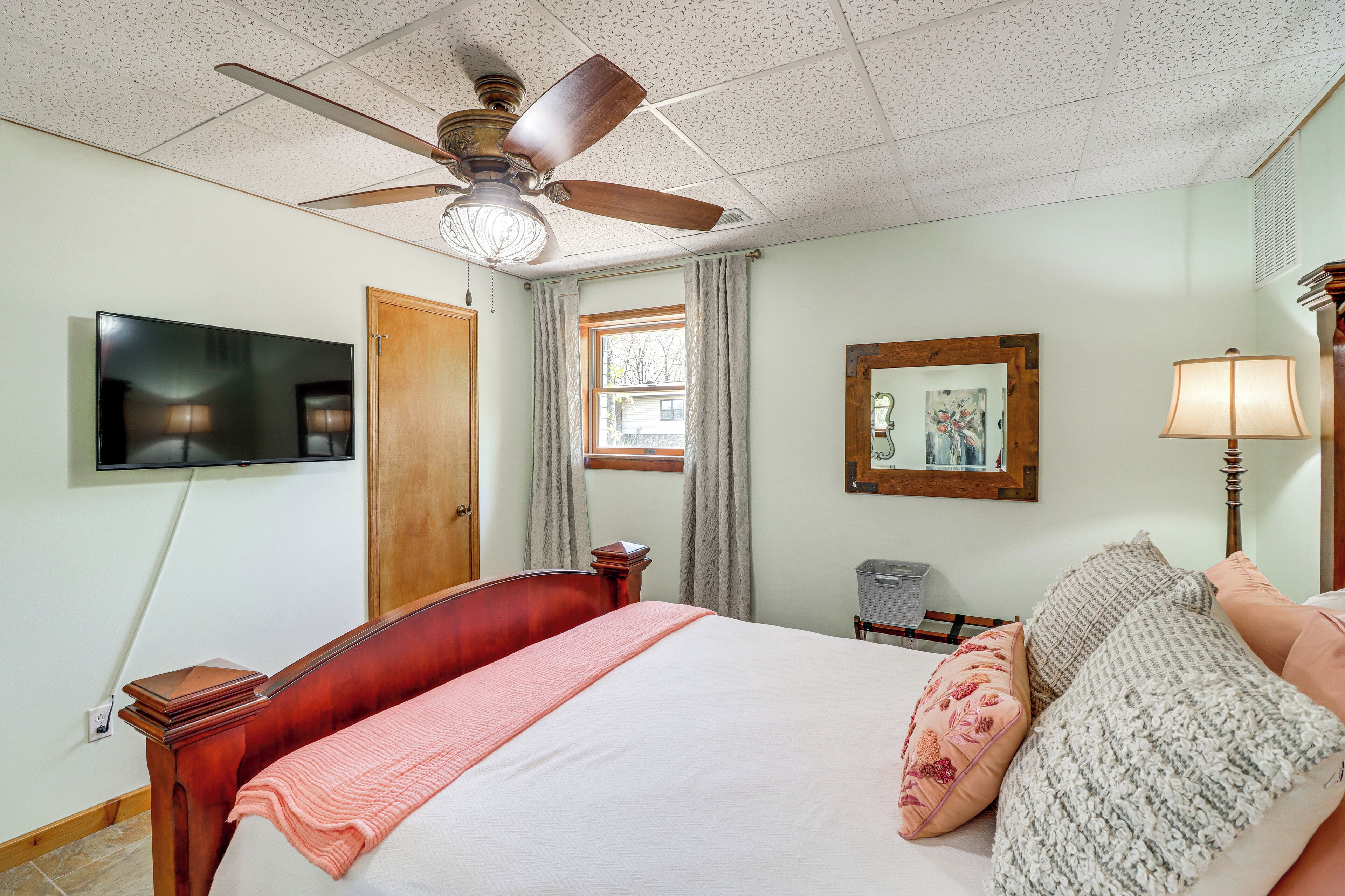 A bedroom with a bed, a ceiling fan, a television, a window with curtains, and a painting on the wall.