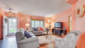 Un salon comprenant un canapé, un fauteuil et un téléviseur, avec un parquet en bois à motifs chevrons et des murs de couleur pêche.