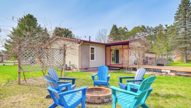 Une maison avec un foyer extérieur et quatre chaises Adirondack dans le jardin.