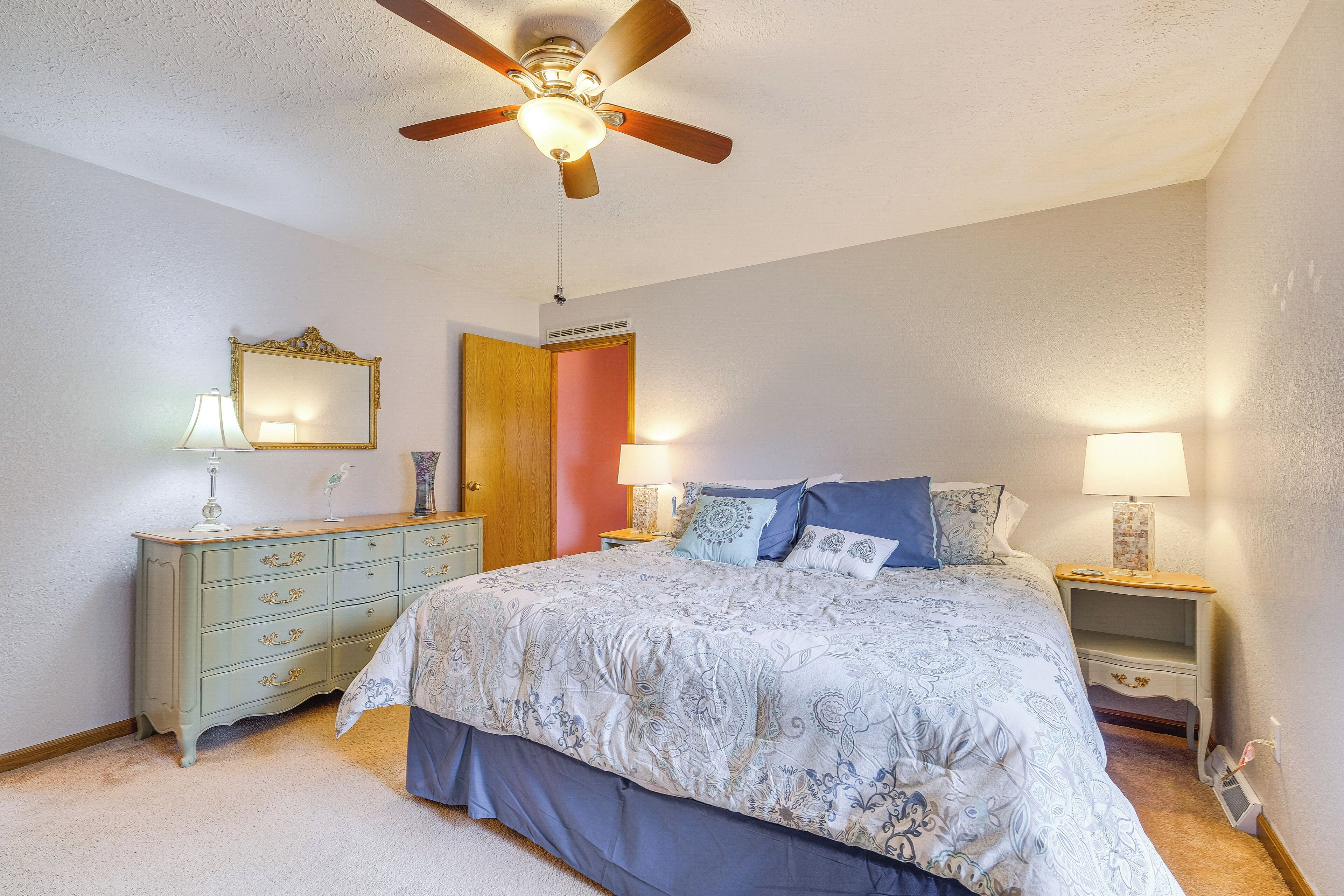 A bedroom with a bed, a dresser, a mirror, a ceiling fan, and two bedside tables with lamps.