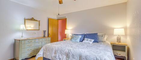 A bedroom with a bed, a dresser, a mirror, a ceiling fan, and two bedside tables with lamps.