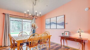 Un coin repas avec une table et des chaises en bois, un lustre, un tableau au mur et une console sur laquelle est posée une lampe.