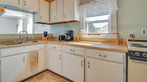 A compact kitchen with white cabinets, a wooden countertop, a coffee maker, and a stove. - Oakland Apt on Messalonskee Lake w/ Dock Access! (Oakland)