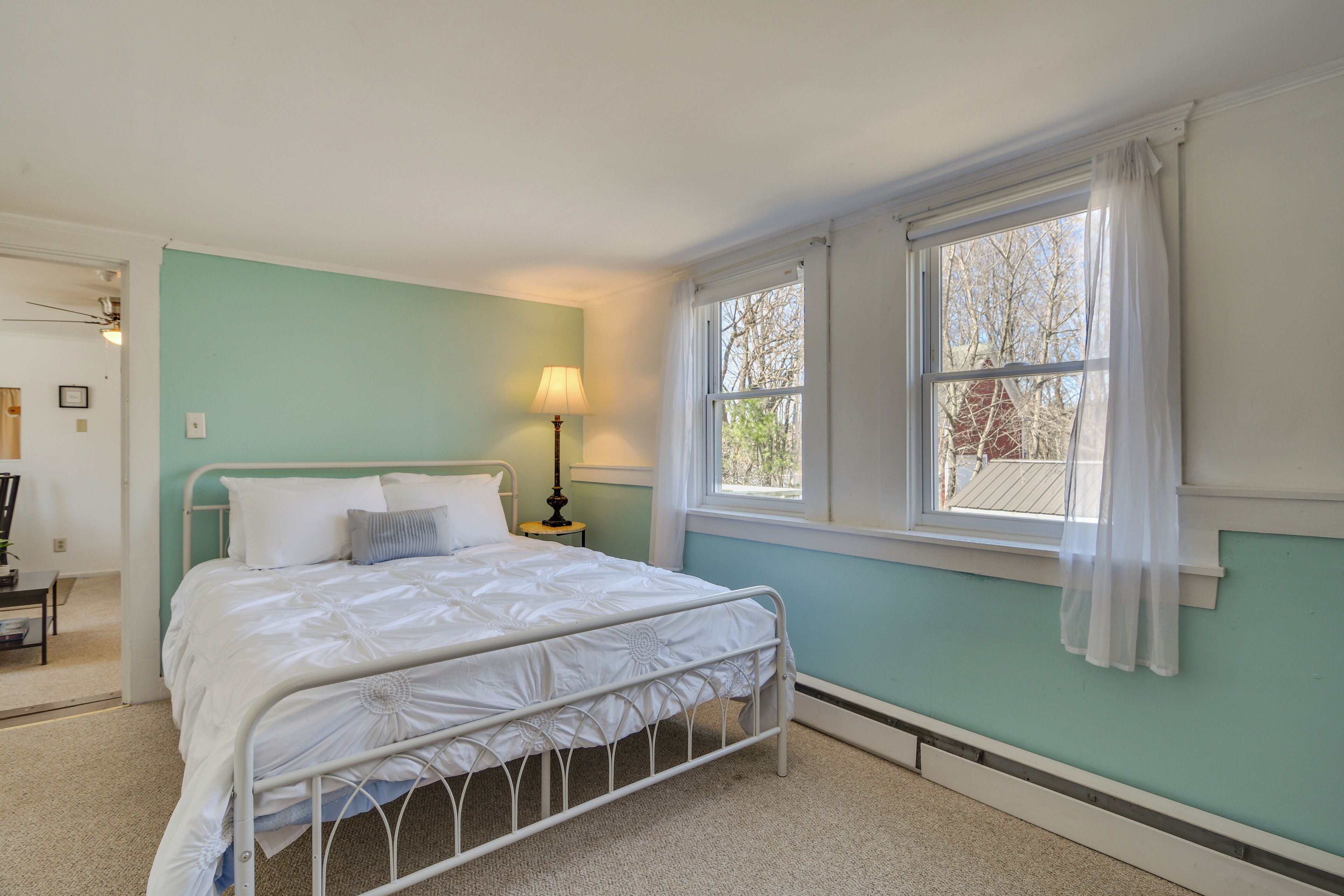 Un dormitorio con cama, mesita de noche, lámpara y ventana con cortinas.