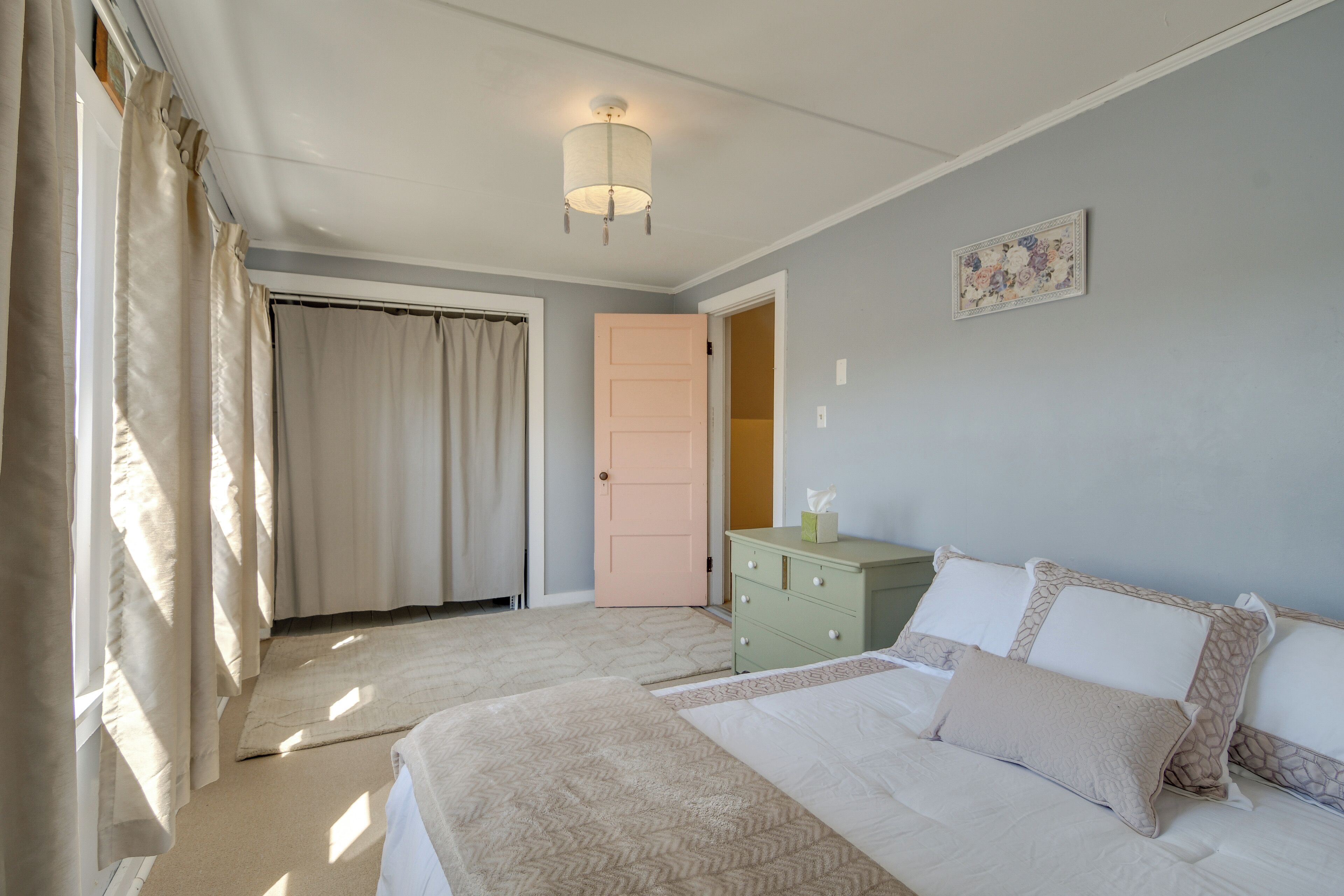 Un dormitorio con cama, cómoda, puerta y una lámpara en el techo.