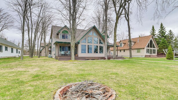 A two-story house with a large front porch, a fire pit in the yard, and a well-maintained lawn. - Family-friendly Houghton Lake House: Steps to Lake (Houghton Lake)