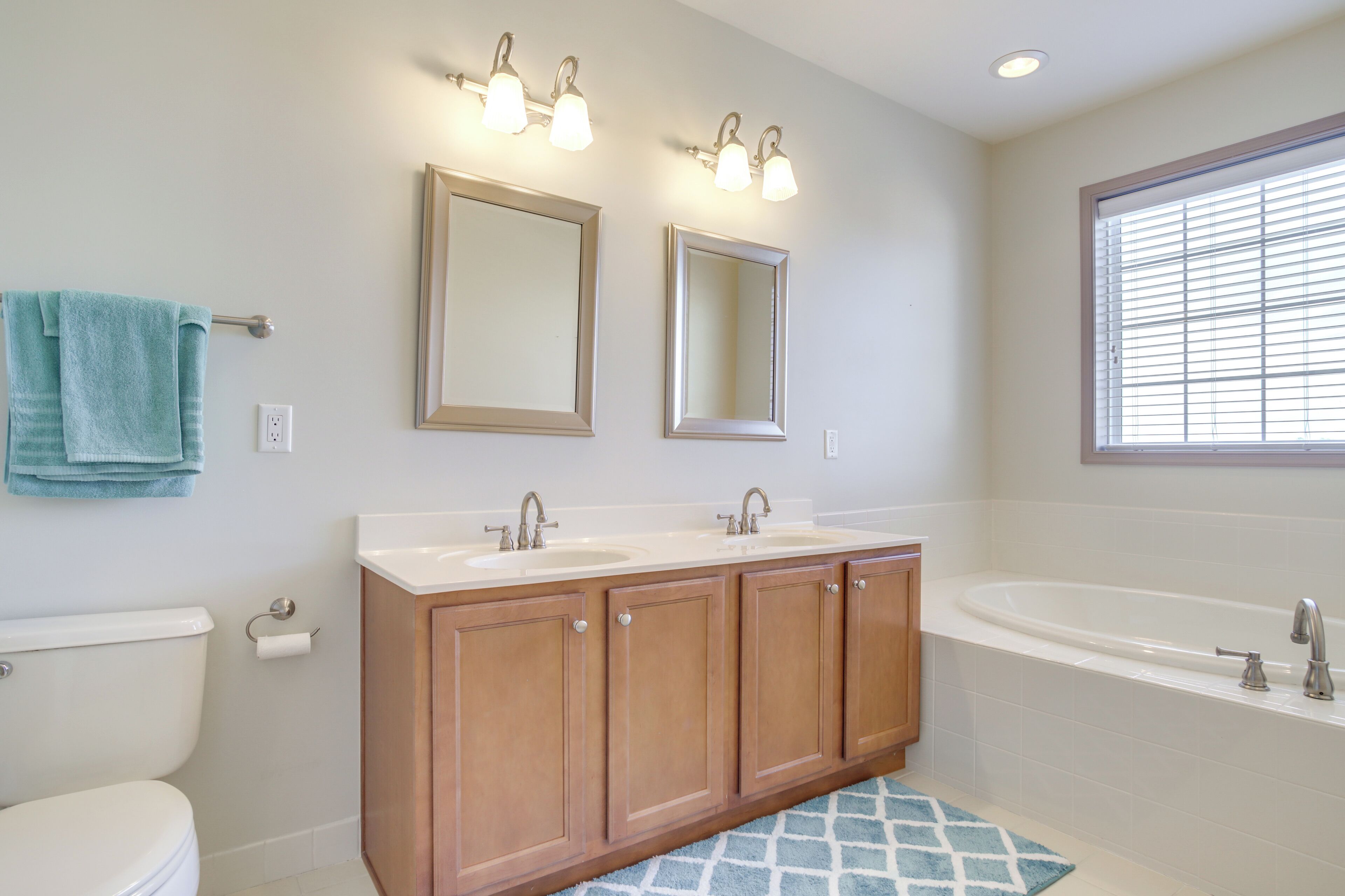 A bathroom with two sinks, a bathtub, wooden cabinets, and a window with blinds.