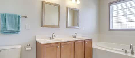 A bathroom with two sinks, a bathtub, wooden cabinets, and a window with blinds.