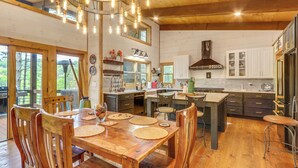 Une table à manger en bois avec des chaises, une cuisine avec des meubles blancs et un luminaire suspendu.