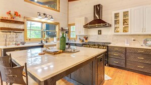 Une cuisine dotée d’un grand îlot central, de meubles blancs, d’une hotte en acier inoxydable et d’un plancher en bois.