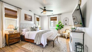 Un dormitorio con cama, mesitas de noche, un banco, un escritorio y un ventilador de techo.