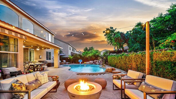Un patio exterior con un hogar para la chimenea, una zona de estar y una piscina.
