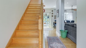 Un escalier en bois mène à un espace de vie où se trouvent un seau vert, un canapé gris et un tapis à motifs.