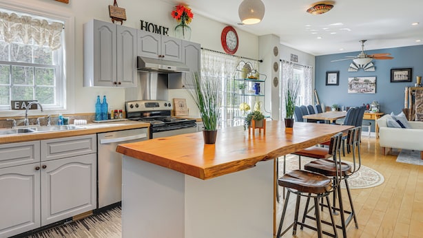 Une cuisine moderne avec un îlot central en bois, des tabourets de bar et un coin repas comprenant un canapé blanc et des chaises bleues.