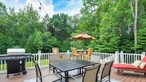 Une terrasse avec un barbecue, une table à manger, des chaises et un fauteuil de relaxation rouge.