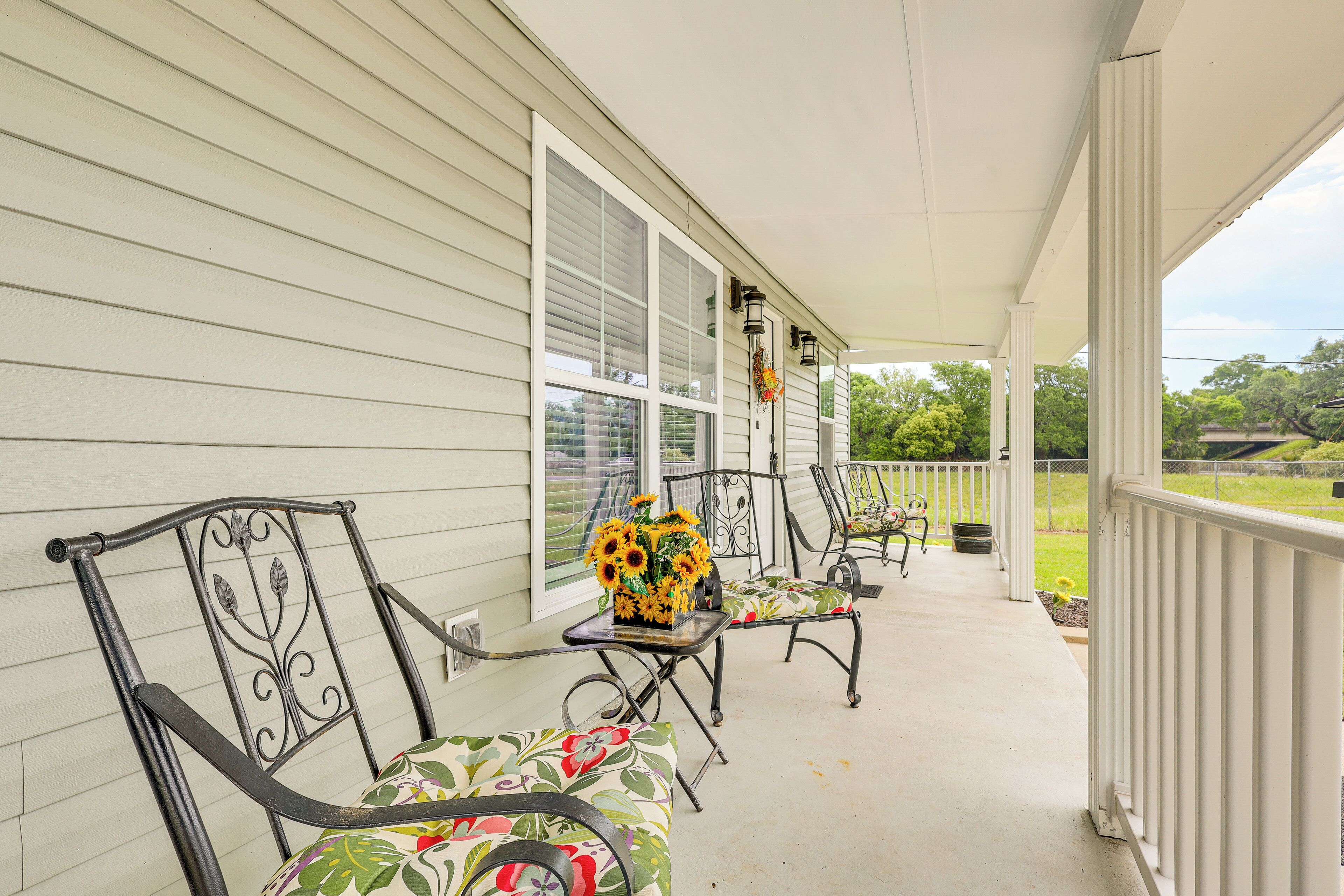 A covered porch with two chairs and a table, a vase of sunflowers, and a view of a green landscape.