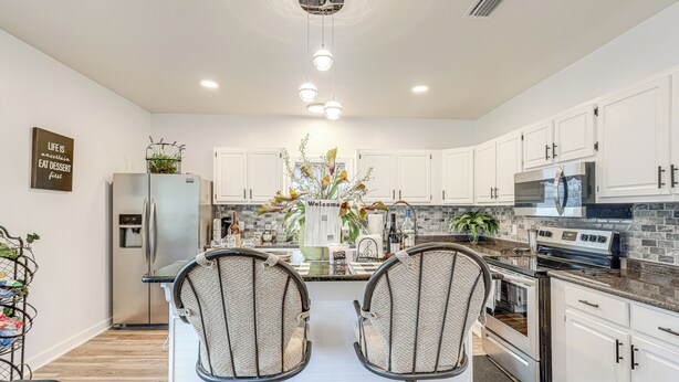 A modern kitchen with white cabinets, stainless steel appliances, and a central island with two bar stools. - Pensacola Home on 1 Acre w/ Large Yard & Grill! (Pensacola)