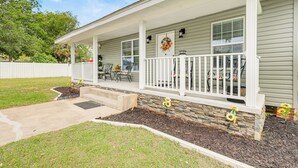 A single-story house with a covered porch, a stone accent wall, and a small garden with sunflowers. - Pensacola Home on 1 Acre w/ Large Yard & Grill! (Pensacola)