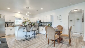 A modern kitchen with white cabinets, a central island, and a dining area with four chairs. - Pensacola Home on 1 Acre w/ Large Yard & Grill! (Pensacola)