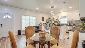 A modern kitchen with white cabinets, a granite countertop, and a dining area with a glass table and brown upholstered chairs. - Pensacola Home on 1 Acre w/ Large Yard & Grill! (Pensacola)