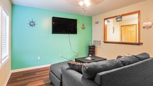 Ein Wohnzimmer mit türkisfarbenen Wänden, einem grauen Sofa, einem flachbildfernseher an der Wand und einem Deckenventilator.