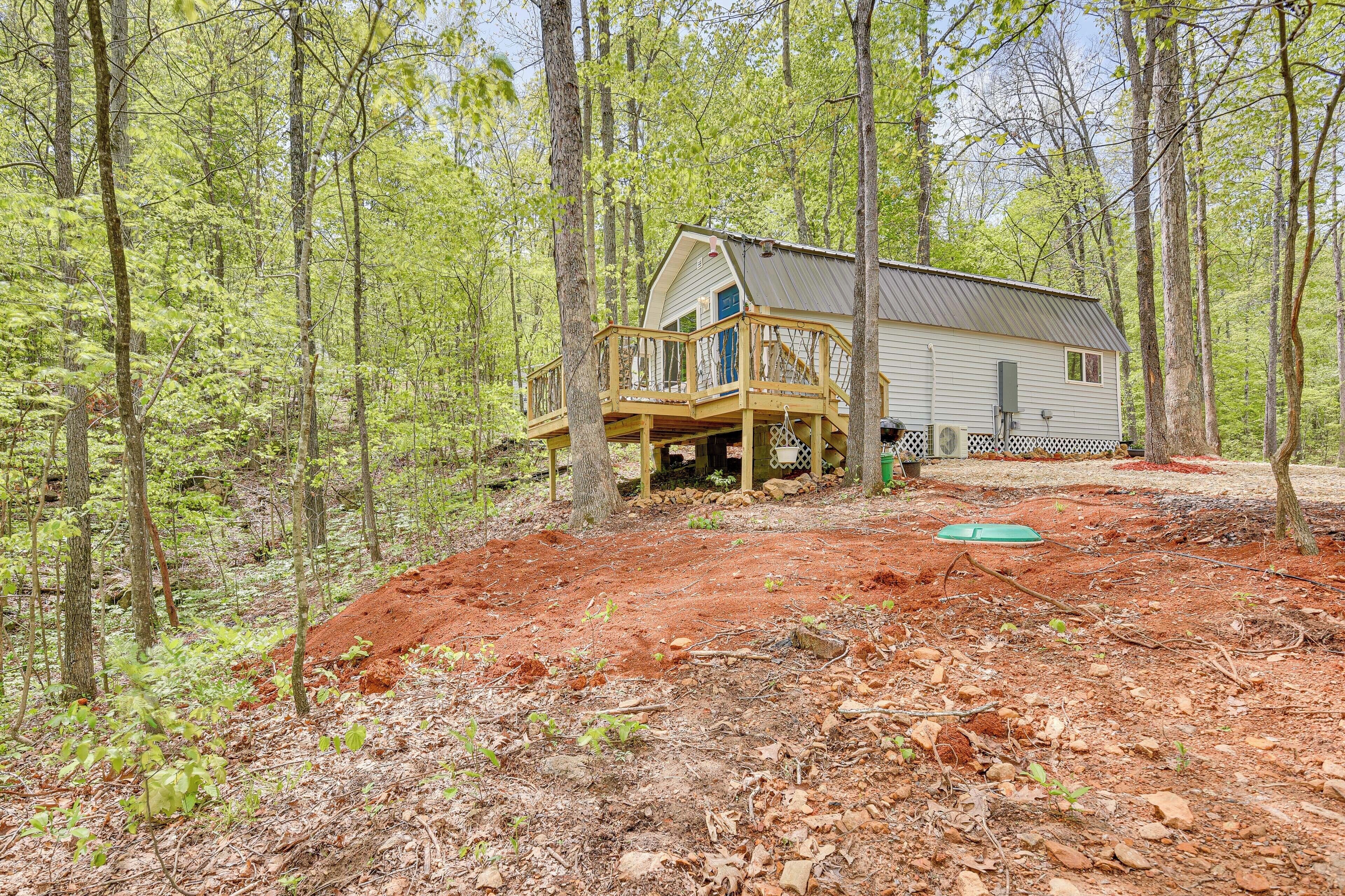 A cabin with a wooden deck and a covered porch, surrounded by a forest.