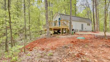 A cabin with a wooden deck and a covered porch, surrounded by a forest.