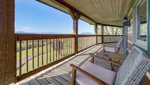 A wooden deck with a view of the landscape, a railing, and a few wicker chairs.