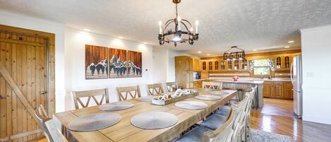A spacious dining area with a long wooden table, multiple chairs, and a chandelier.