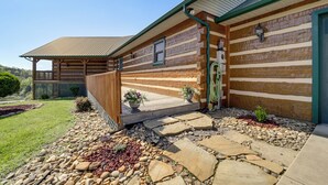 A log cabin with a covered porch, stone pathway, and potted plants.