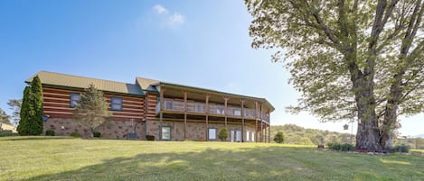 A large, two-story log cabin with a balcony and a stone foundation.