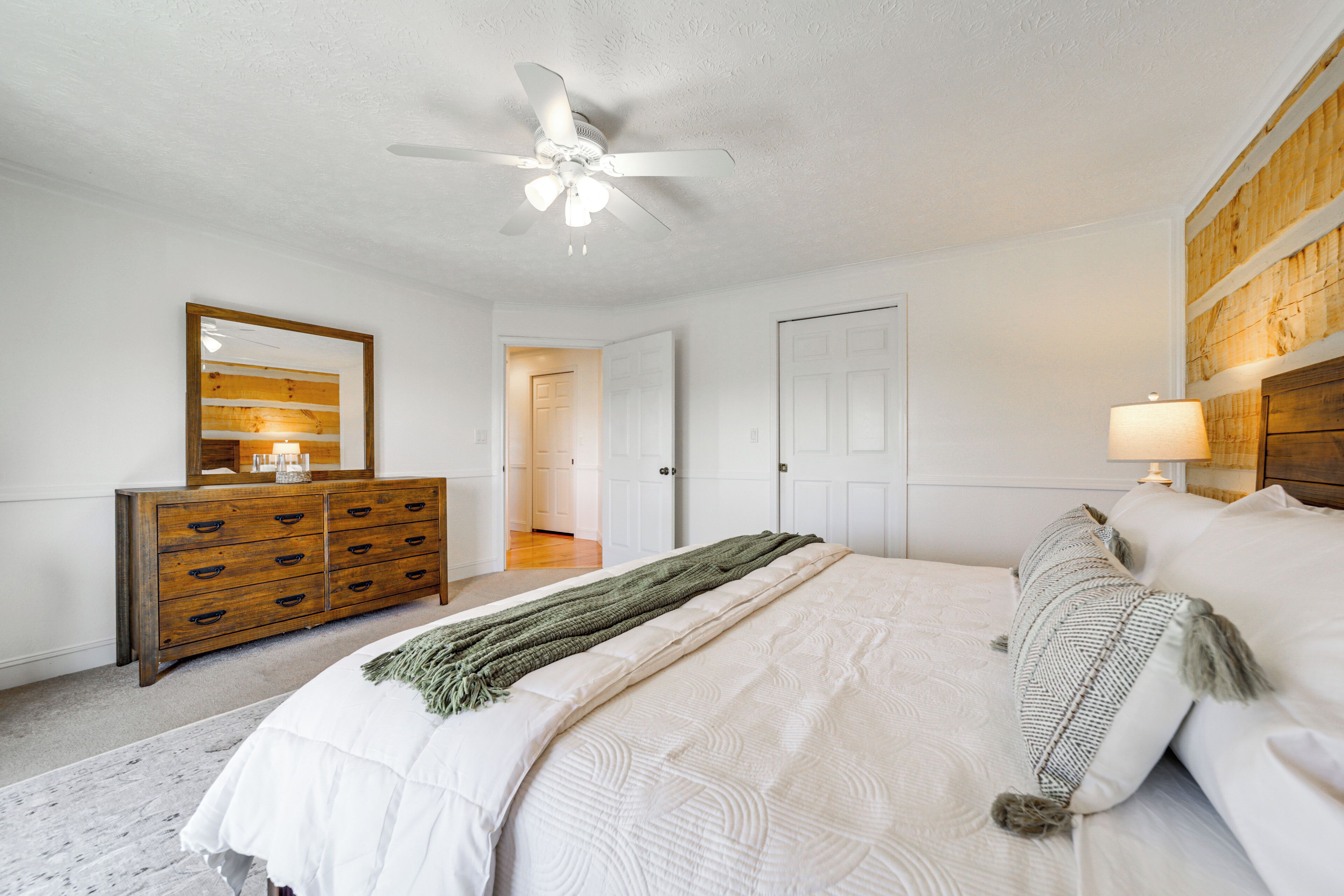 A bedroom with a bed, a dresser, a ceiling fan, and a door leading to another room.