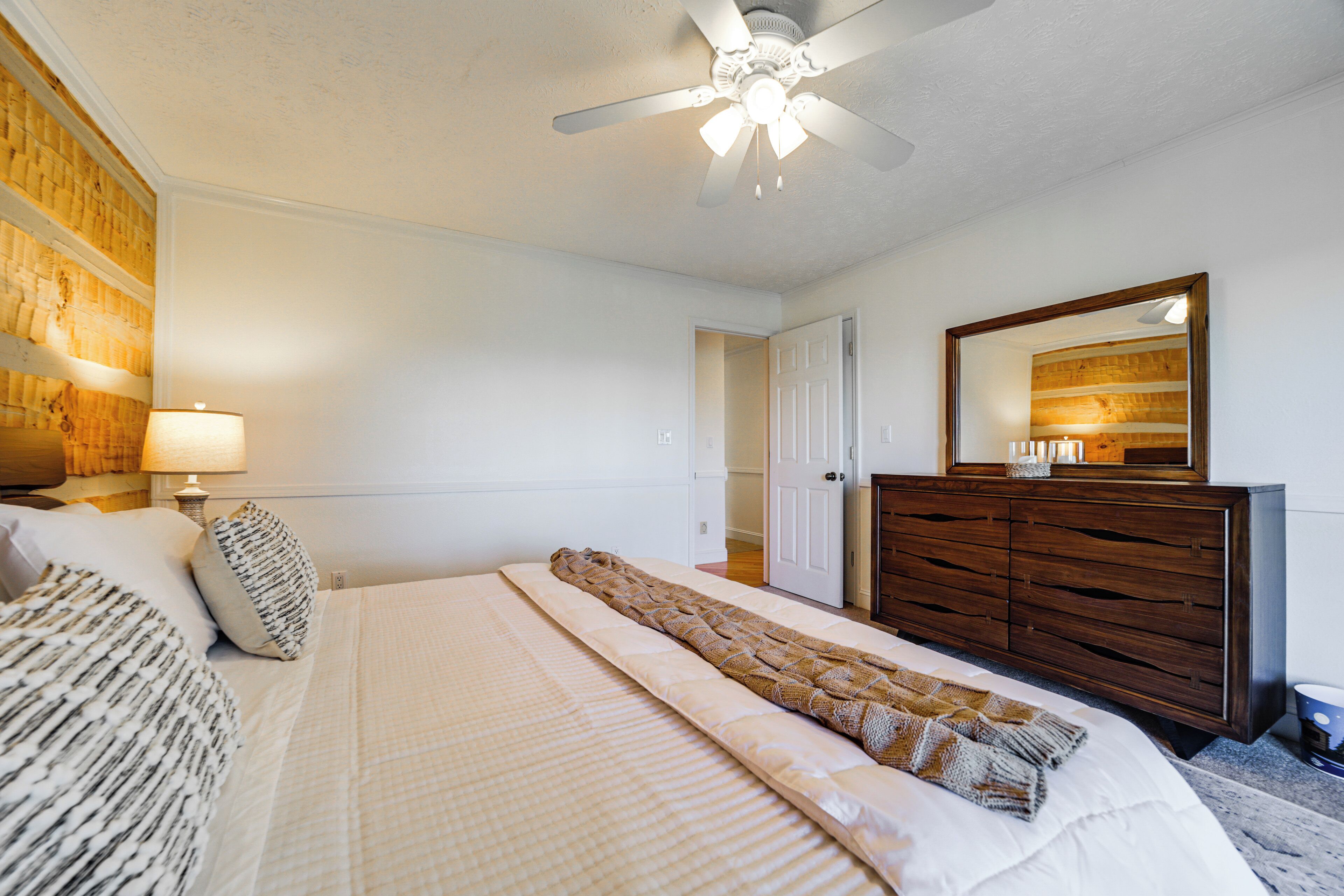 Une chambre à coucher avec un lit, une commode, un ventilateur de plafond et un miroir.