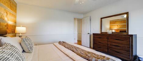Une chambre à coucher avec un lit, une commode, un ventilateur de plafond et un miroir.