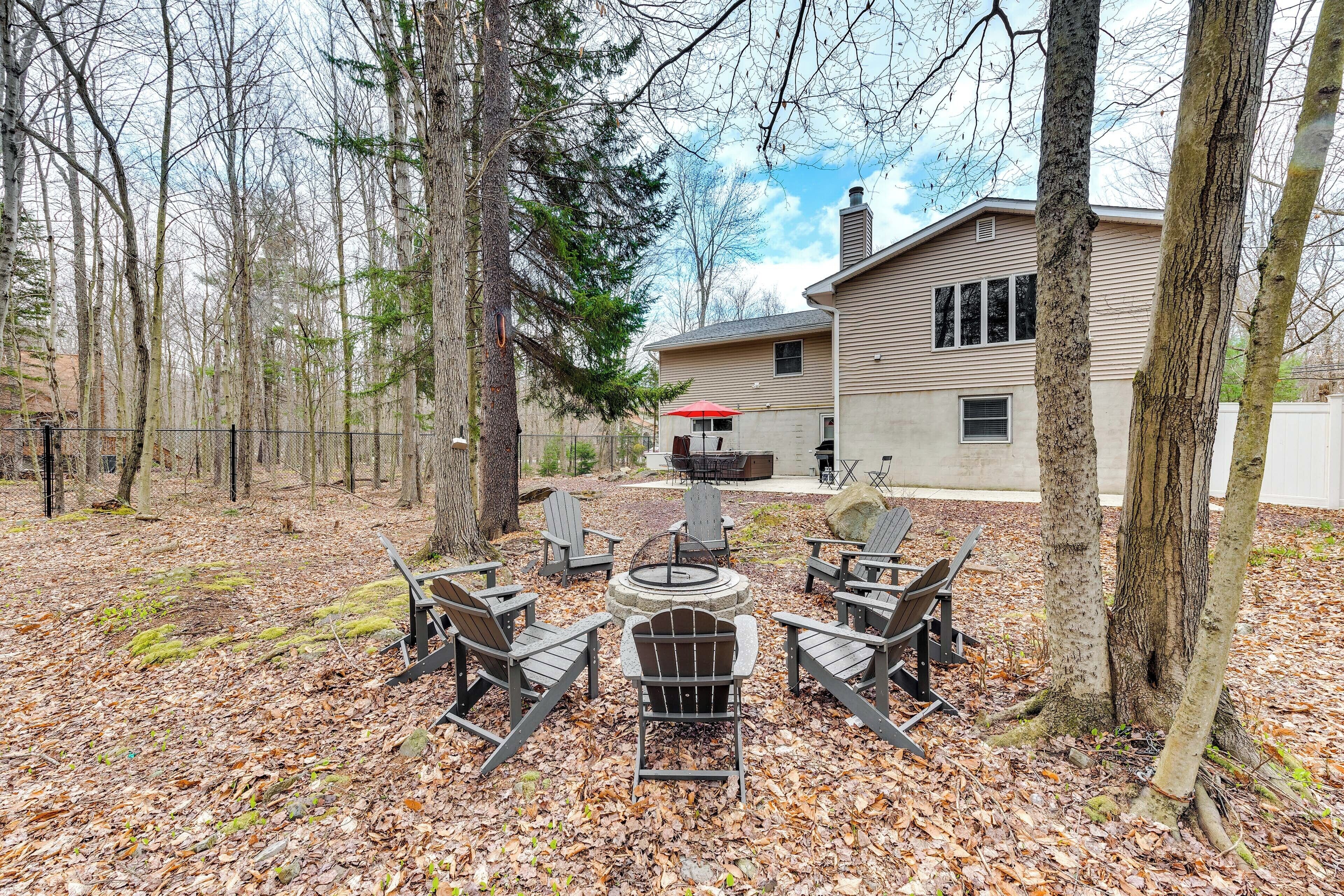 An outdoor seating area with a fire pit, surrounded by trees and a house in the background.