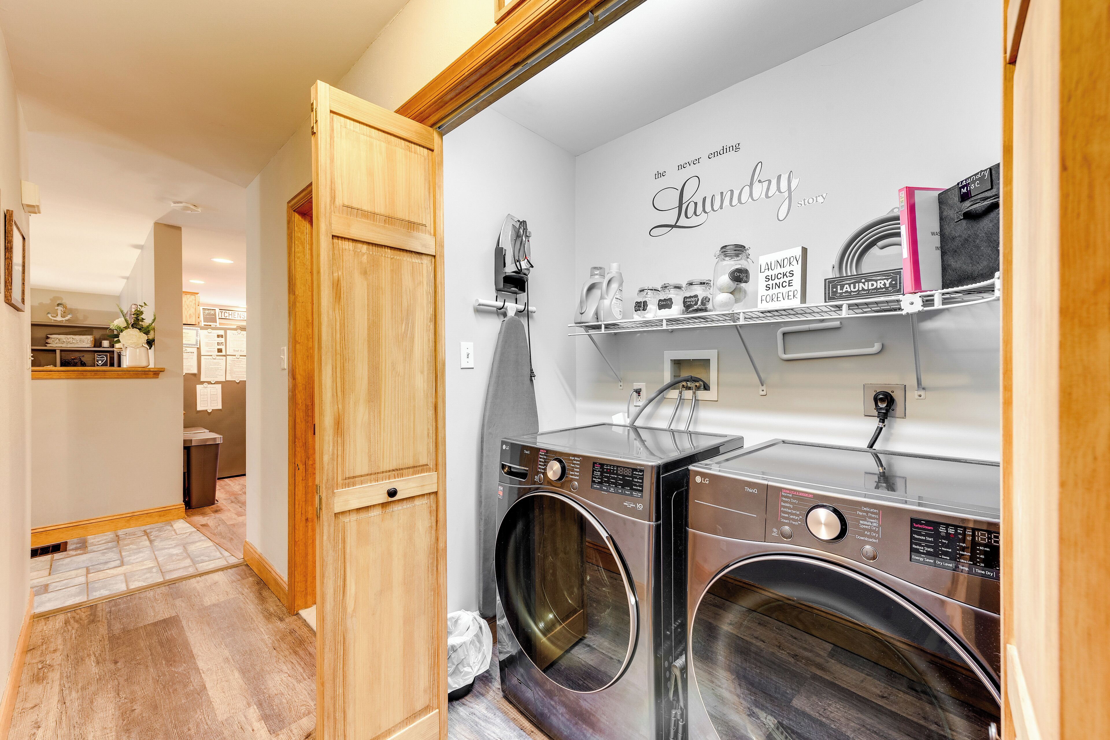 A laundry room with two front-loading washing machines, a drying rack, and a shelf with laundry supplies.